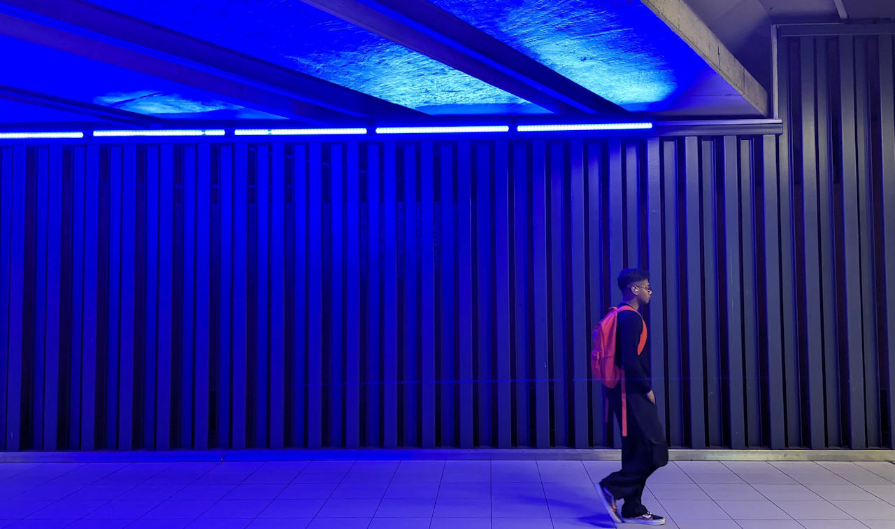 Junger Mann mit rotem Rucksack vor einer blauen Lichtinstallation in der Metro Station Bockstael Brüssel
