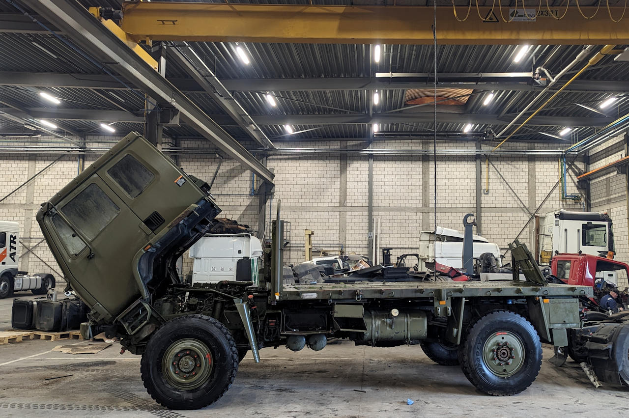 Ein olivgrüner Militär LKW steht mit hochgeklapptem Führerhaus in einer Halle