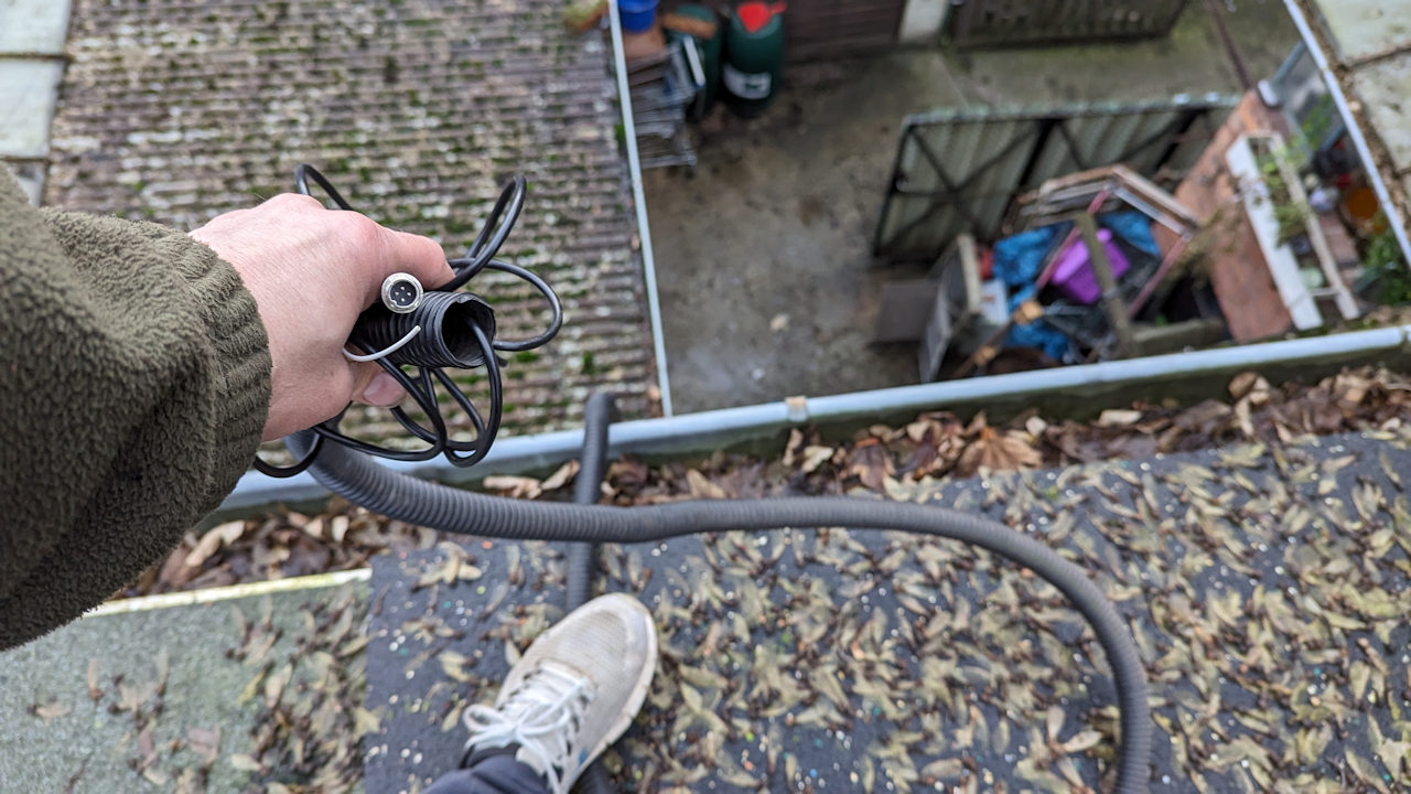 Hand hält schwarzen Plastikschlauch der von einem Dach herunterhängt um ein Kabel einzuführen 