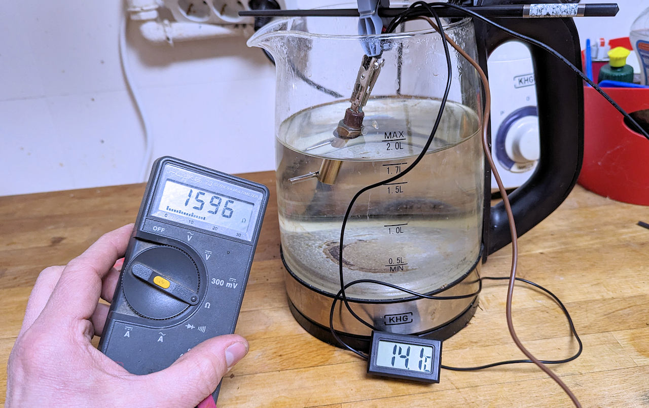 Testaufbau mit einem Thermosensor in einem Wasserkocher, Thermometer und Ohm Messgerät
