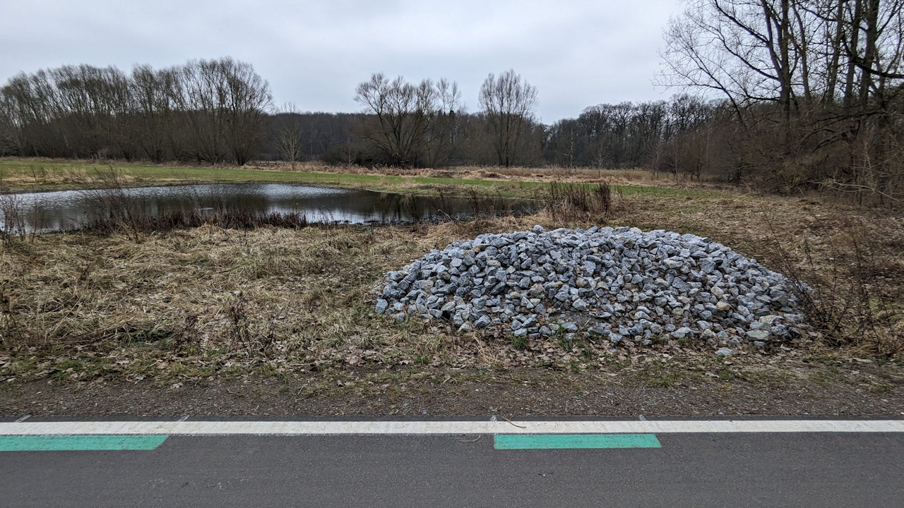 Blick von der Veloroute auf einen Teich und einen Steinhaufen