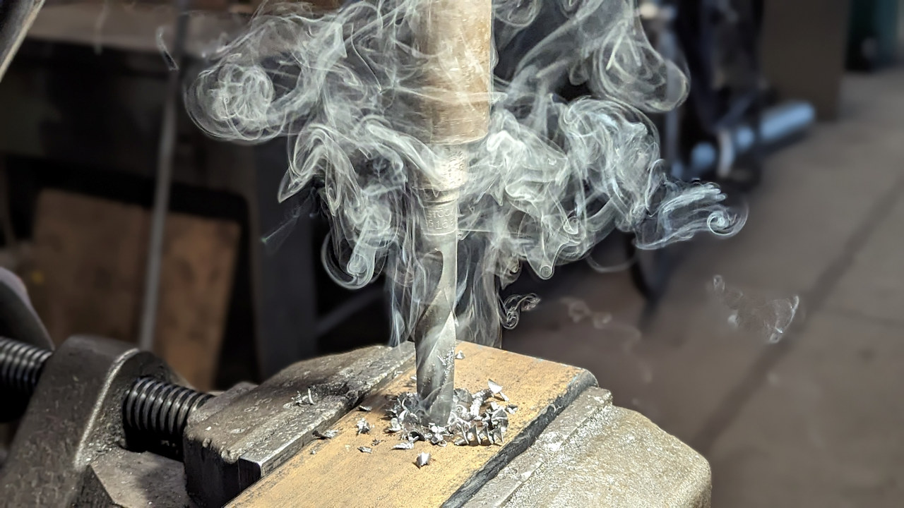 Ein Metallbohrer hebt bei einem Werkstück Späne ab und erzeugt dabei weisse sich kringelnde Rauchwolken