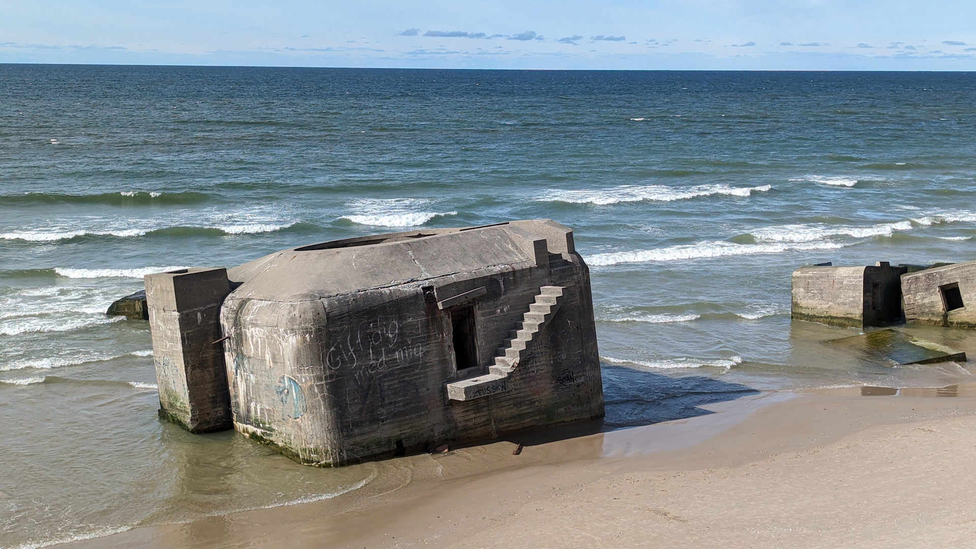 Ein Bunker steht schräg am Strand von  Lökken, Wellen umspülen den Bunker