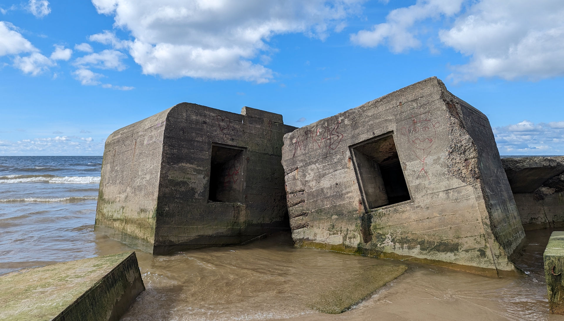 Zwei Bunker stehen halb im Meer und sind im Sand versunken