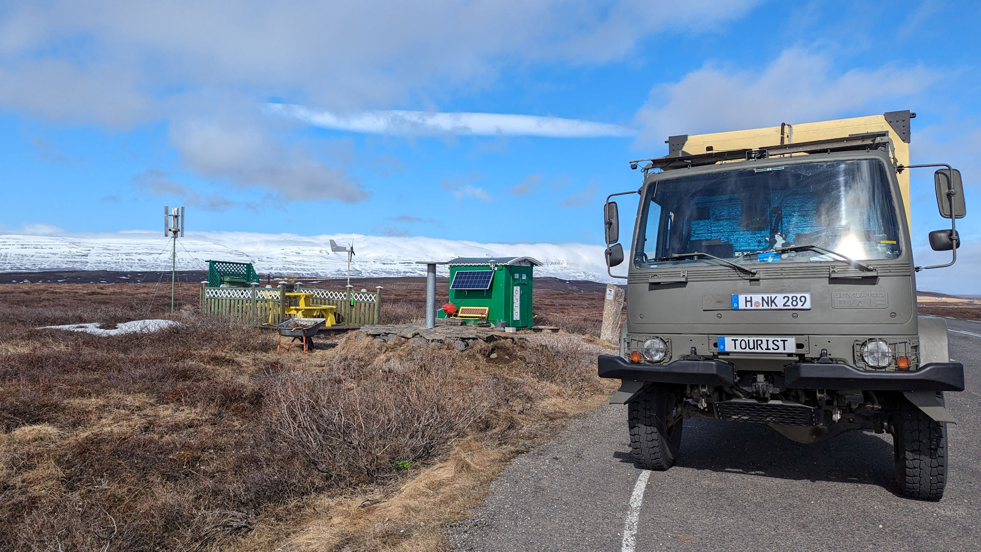 Grüne Hütte für Verkaufsautomaten an der 94 mit davor parkenden DAF T244 LKW, kleinem Picknickplatz und schneebedeckten Bergen im Hintergrund