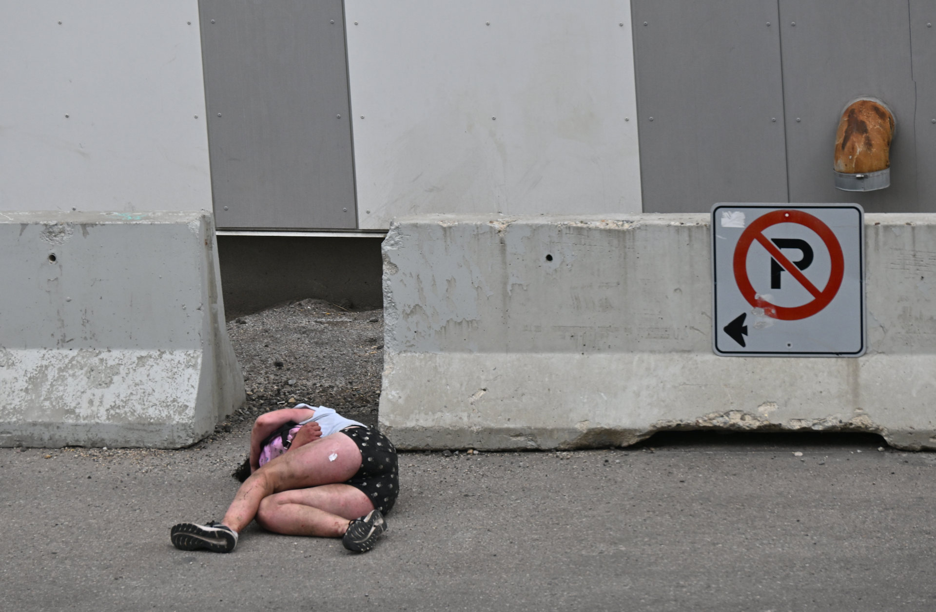 Ein Drogenabhängiger liegt neben einem nicht hier parken Schild mit nackten Beinen bewegungslos auf der Strasse