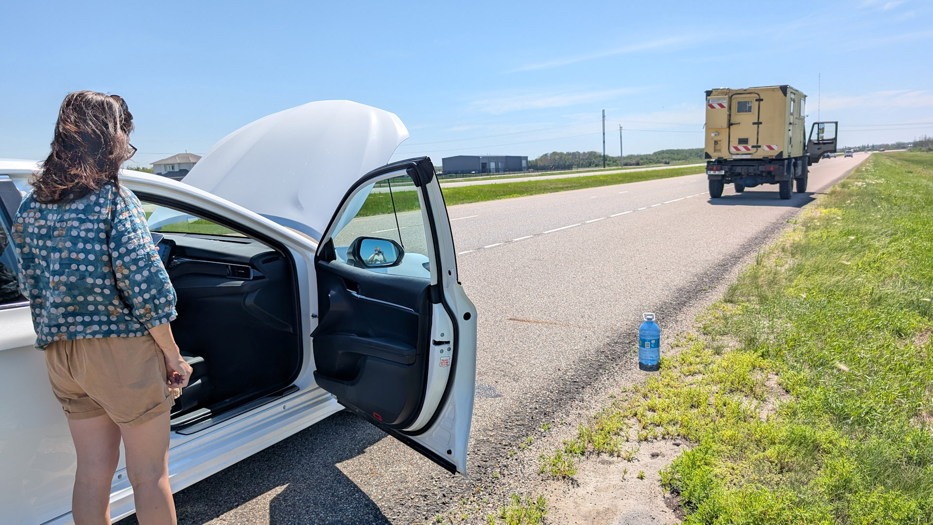 LKW steht auf der Autobahn vor einem Toyota Camry mit geöffneter Motorhaube und einer Wasserflasche am Strassenrand. 