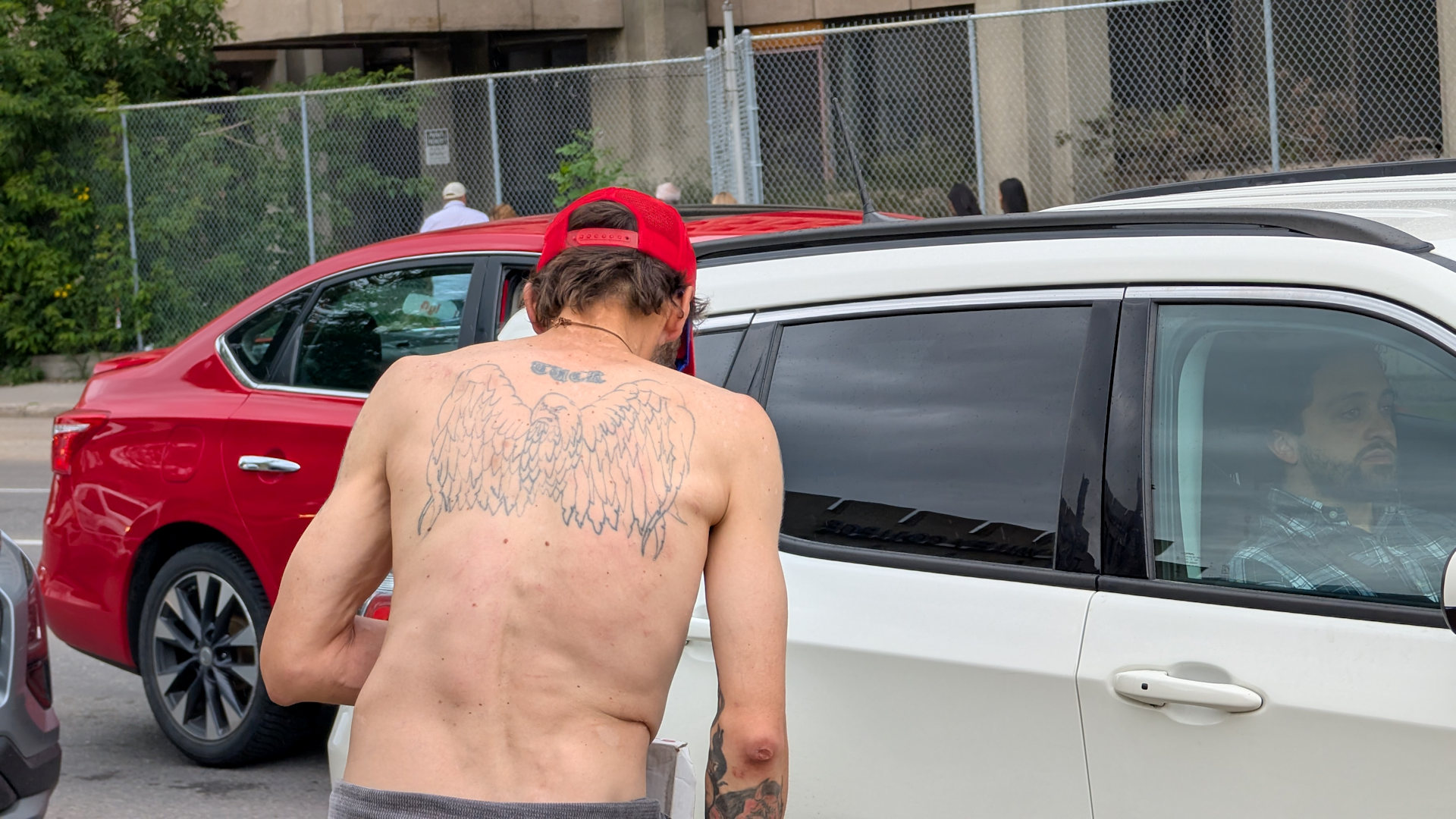Obdachloser mit nacktem Oberkörper und Adler Tatoo auf dem Rücken versucht wartende Autofahrer anzubetteln