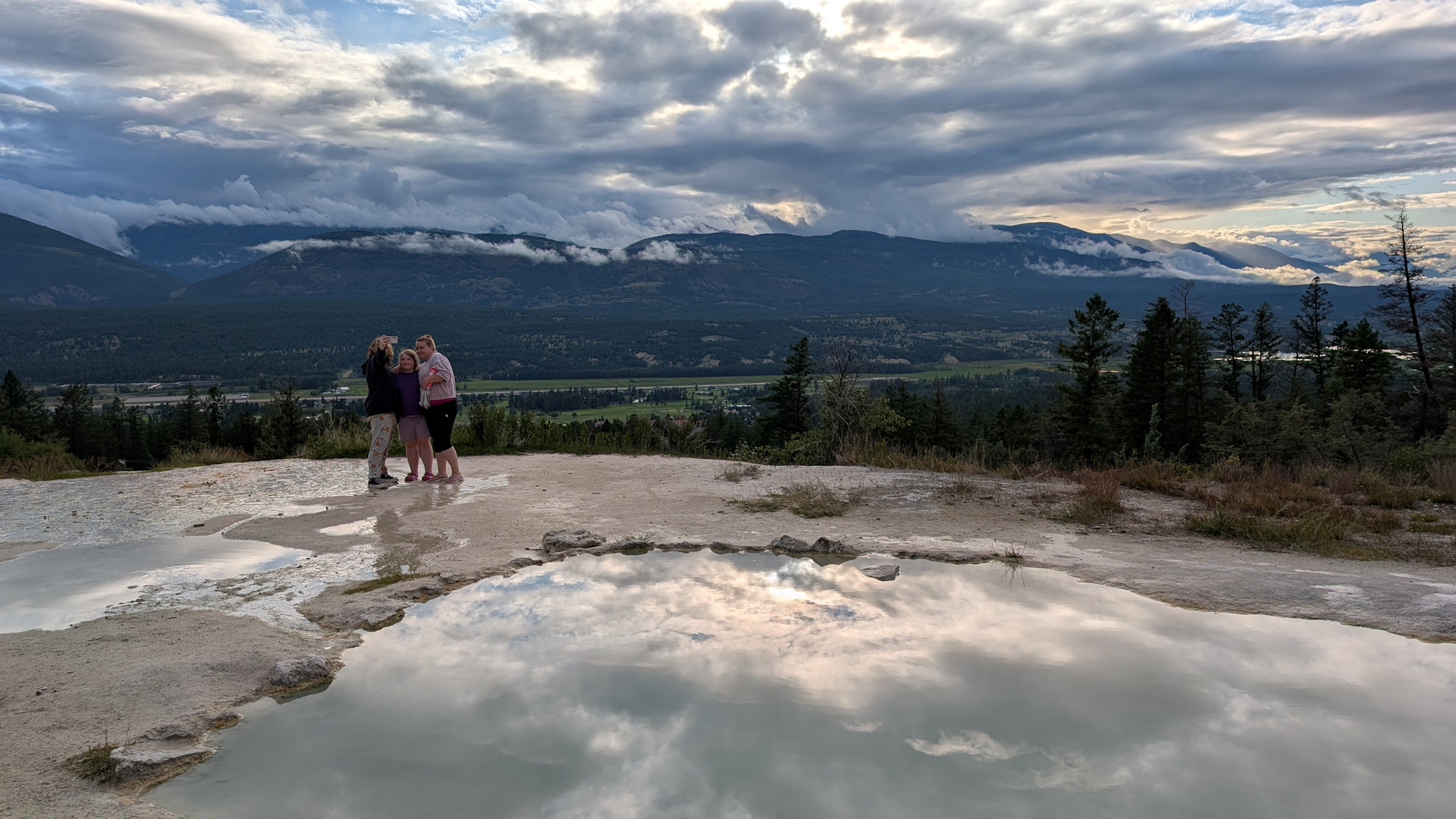 Schlammige Quellen auf dem dem Gelände der Fairmont Hot Springs mit drei Kindern und Bergen im Hintergrund 