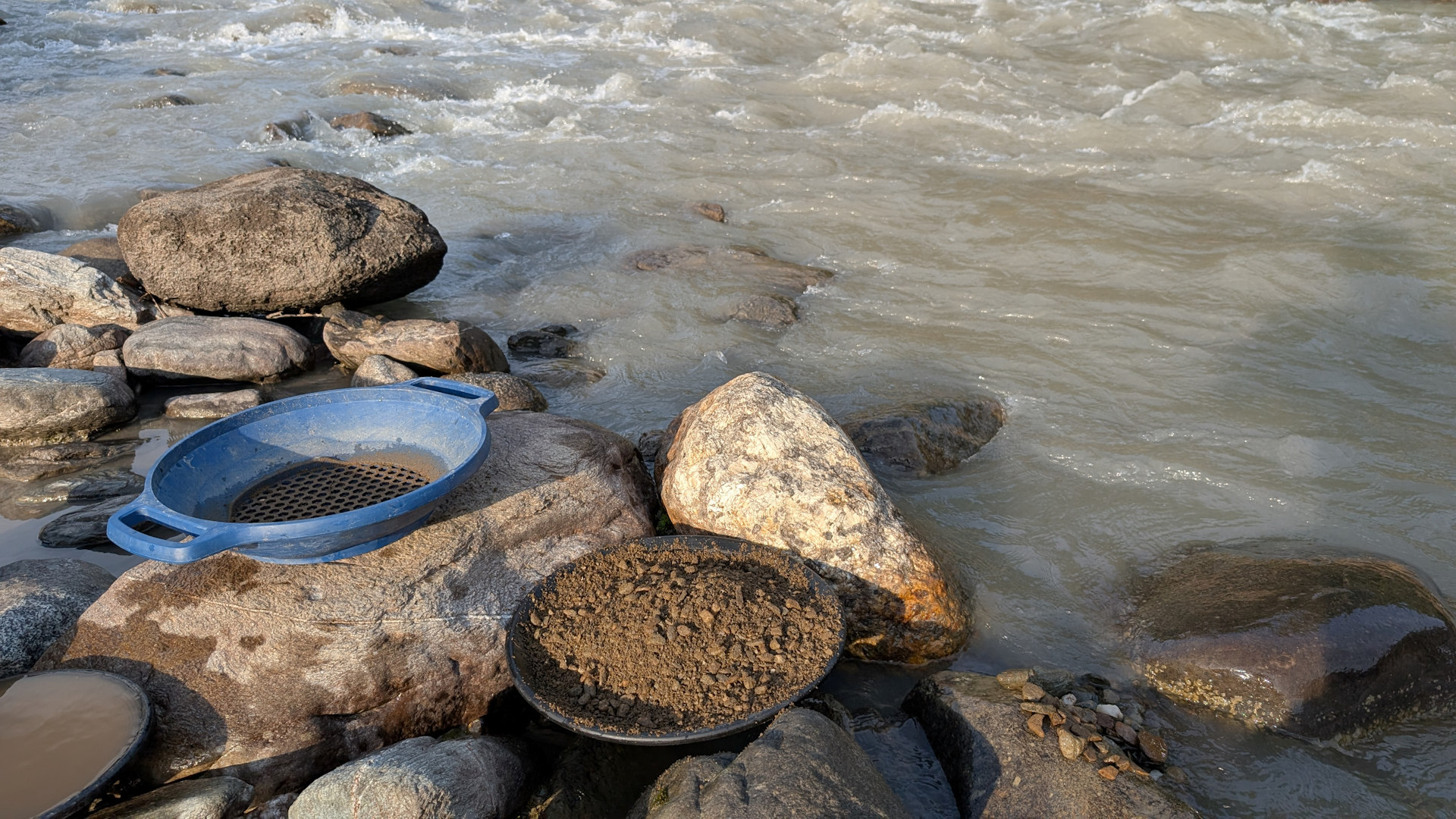 Goldwaschpfanne mit goldhaltigem Kies und Sieb an einem Fluss 