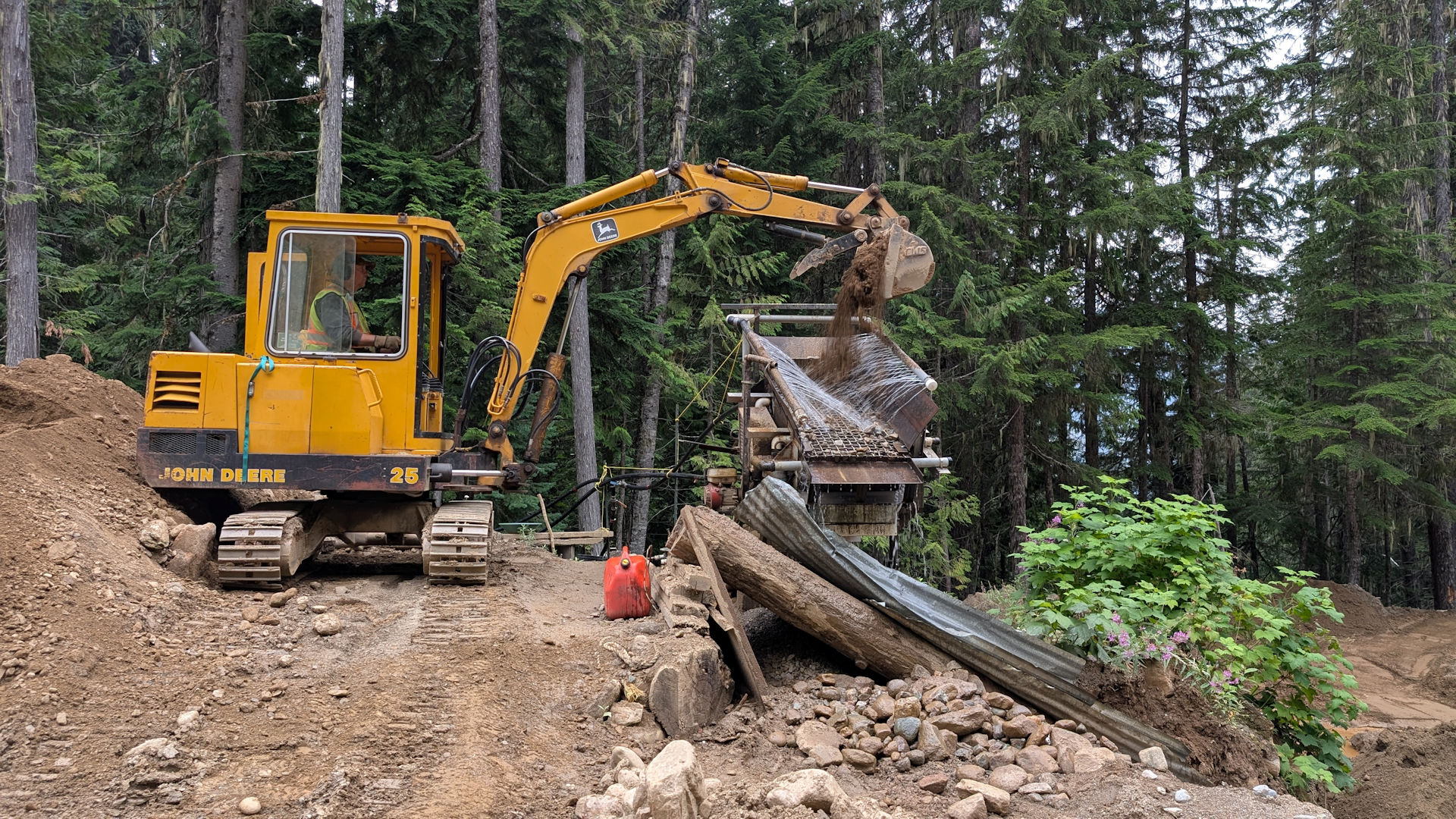 Kleiner John Derre Bagger füllt goldhaltigen Sand in eine Goldwaschanlage