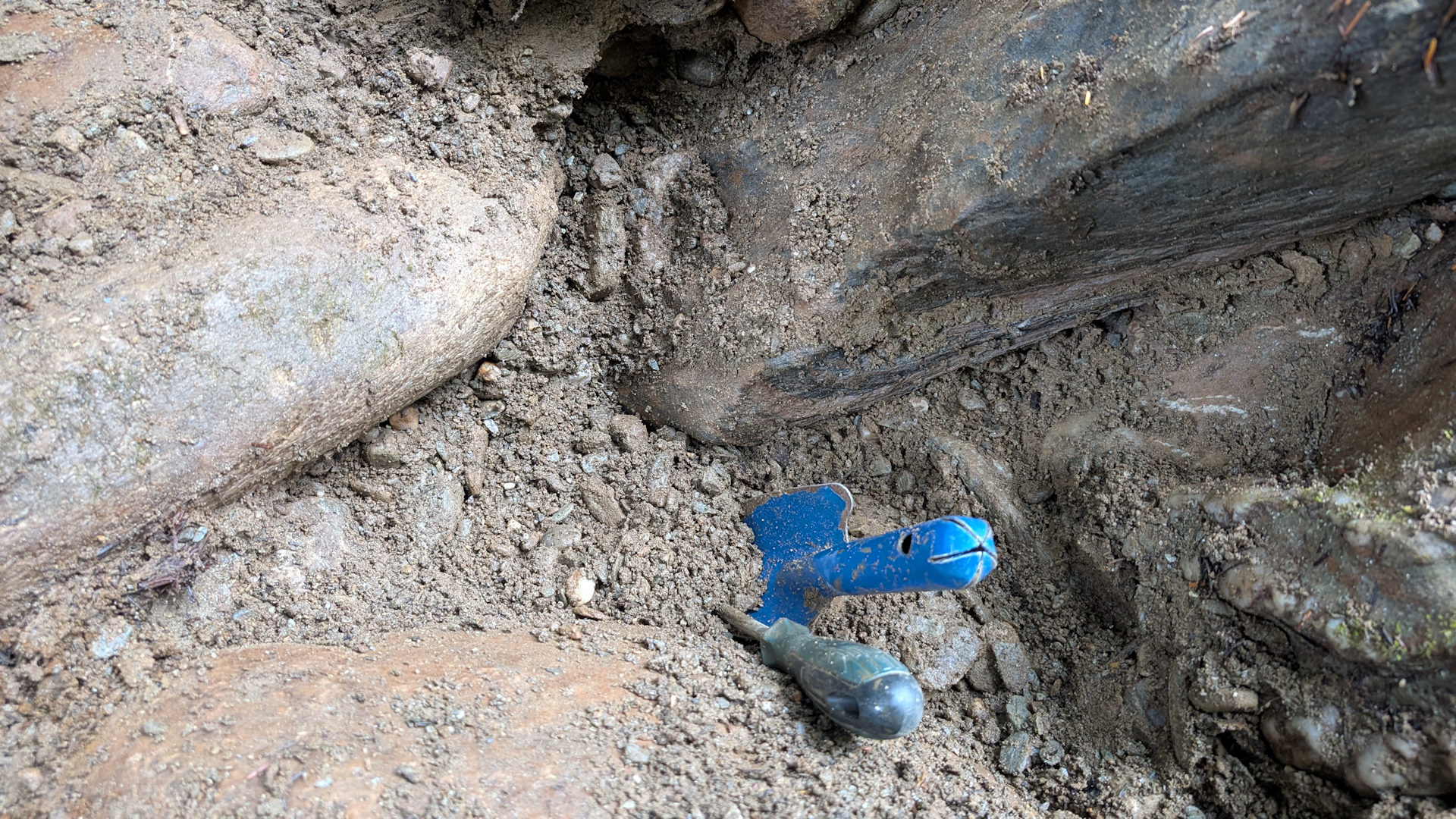 Goldhaltiger Kies zwischen grossen Steinen, Schraubenzieher und blaue Sandschaufel