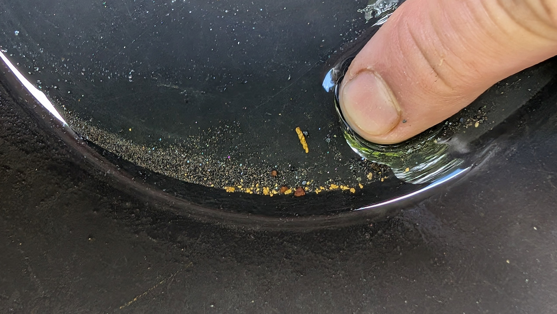 Schwarze Goldwaschpfanne mit stabförmigen Goldnugget