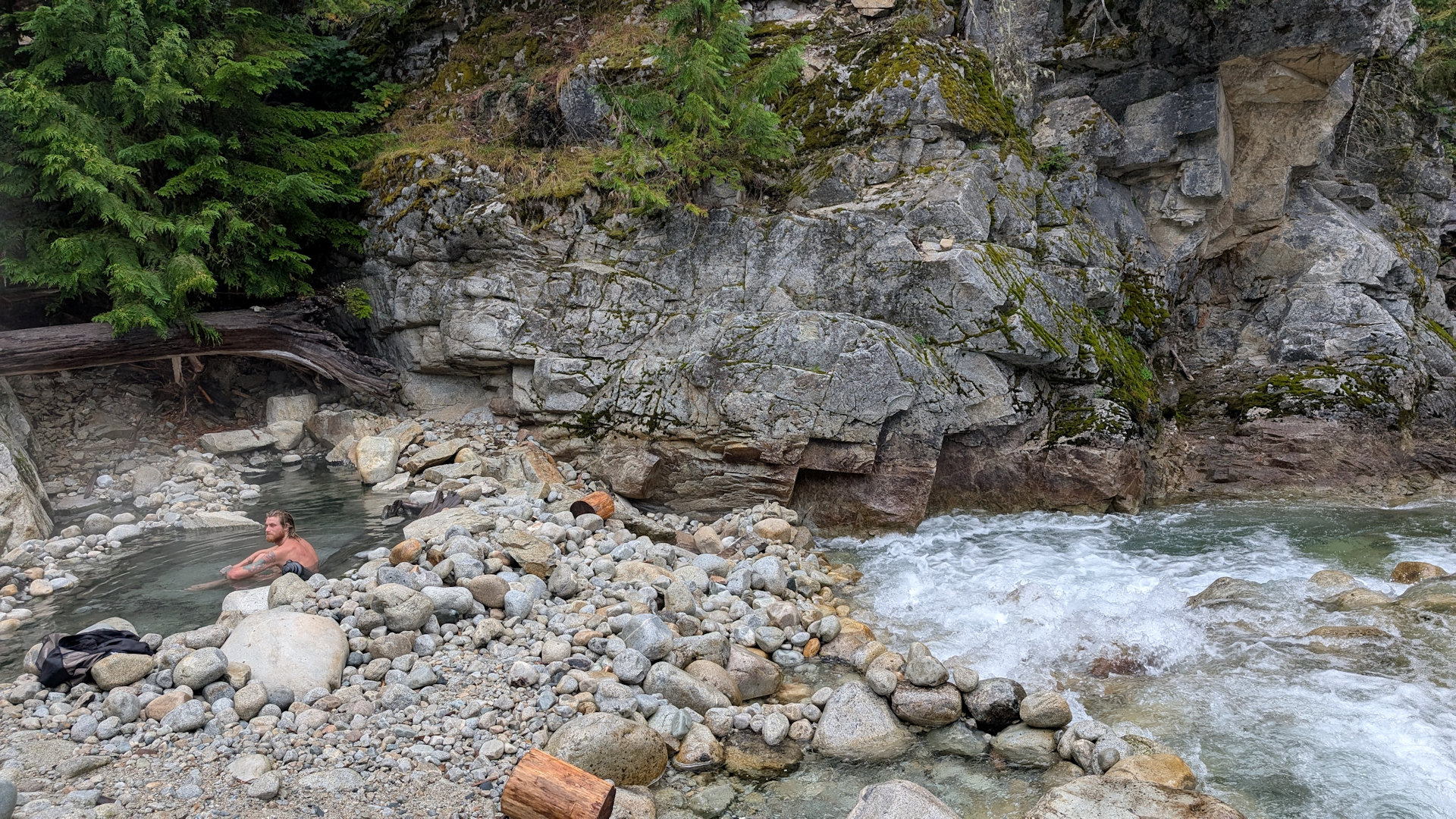 Badebecken der Half Way Hotsprings am Fluss in dem ein Mann sitzt 