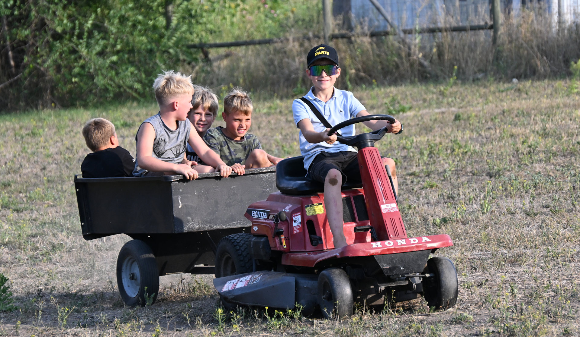 Fünf Kinder fahren auf einem Honda Rasenmäher mit Anhänger 