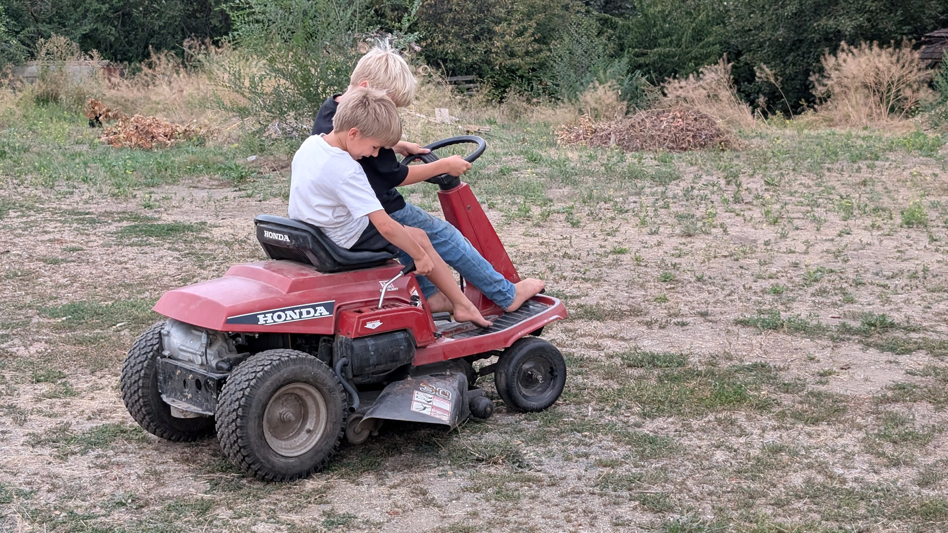 Zwei Kinder auf einem roten Aufsitzrasenmäher von Honda
