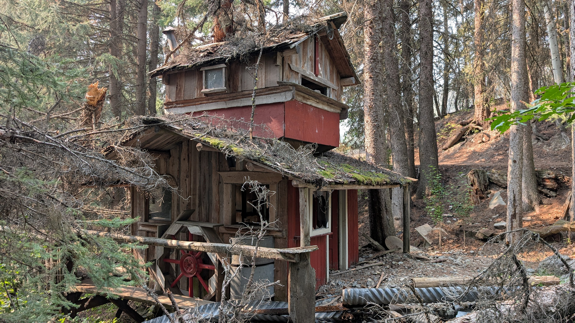 Verfallenes Hexenhaus in den Bergen mit roten Wänden und  Mühlenrad
