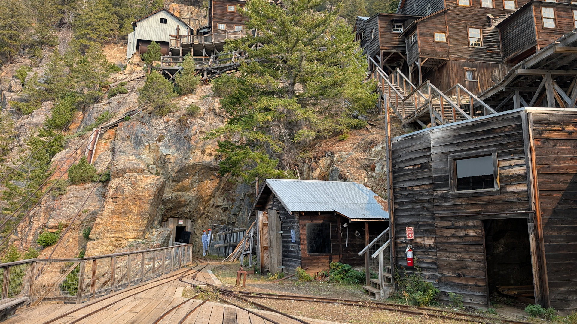 Hauptebene der Mascort Mine mit mehreren Gebäuden aus Holz die in den Hang hinein gebaut sind. Im Hintergrund ist der Eingang vom Stollen 