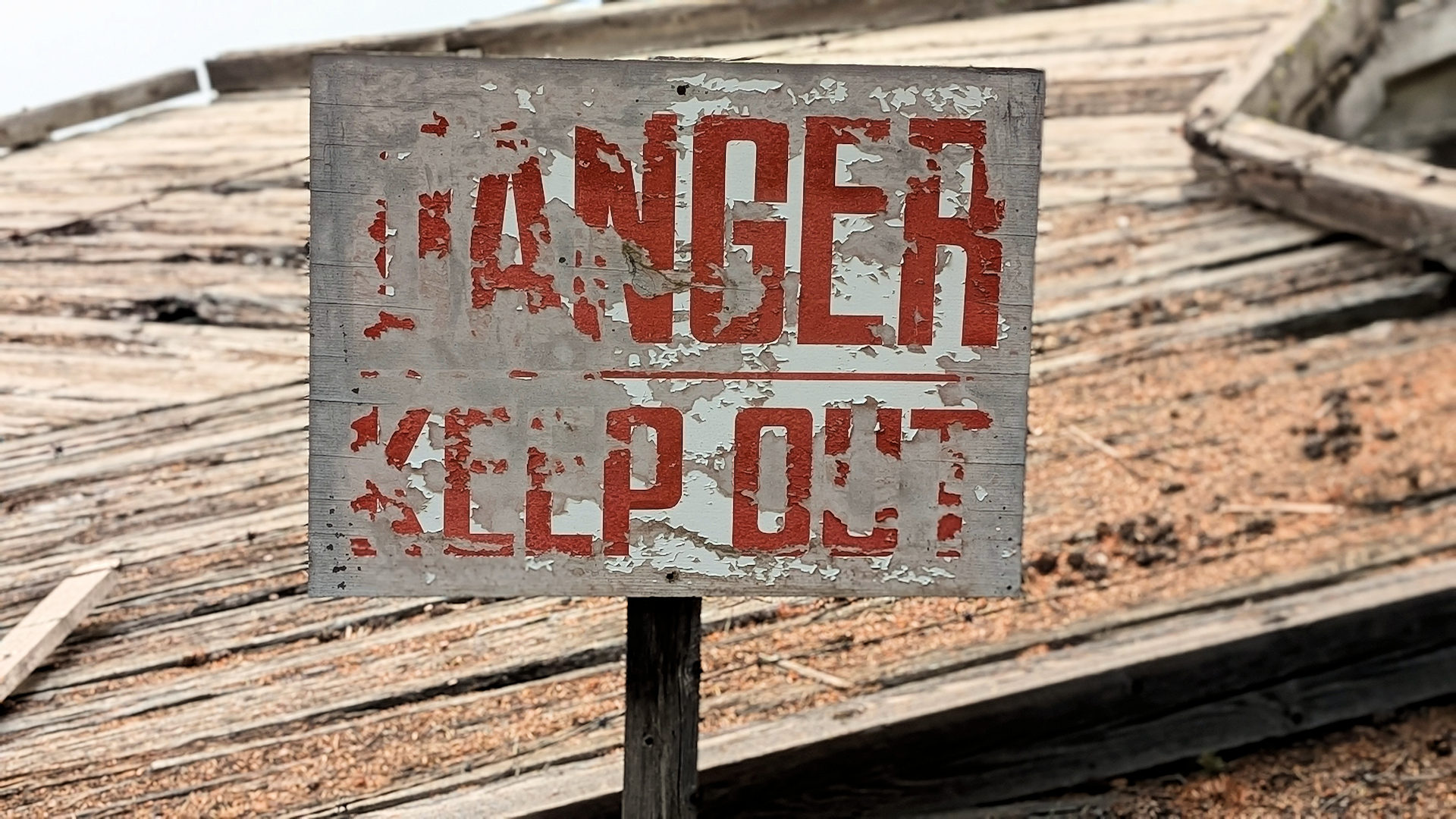 Schild mit abgeblätterten und schwer zu lesenden Danger Keep Out Schriftzug in roter Schrift 