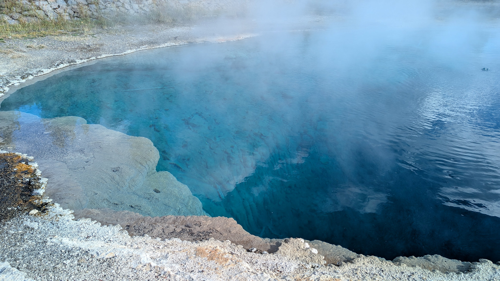 Wasserdampf zieht über eine blau leuchtende Thermalquelle 