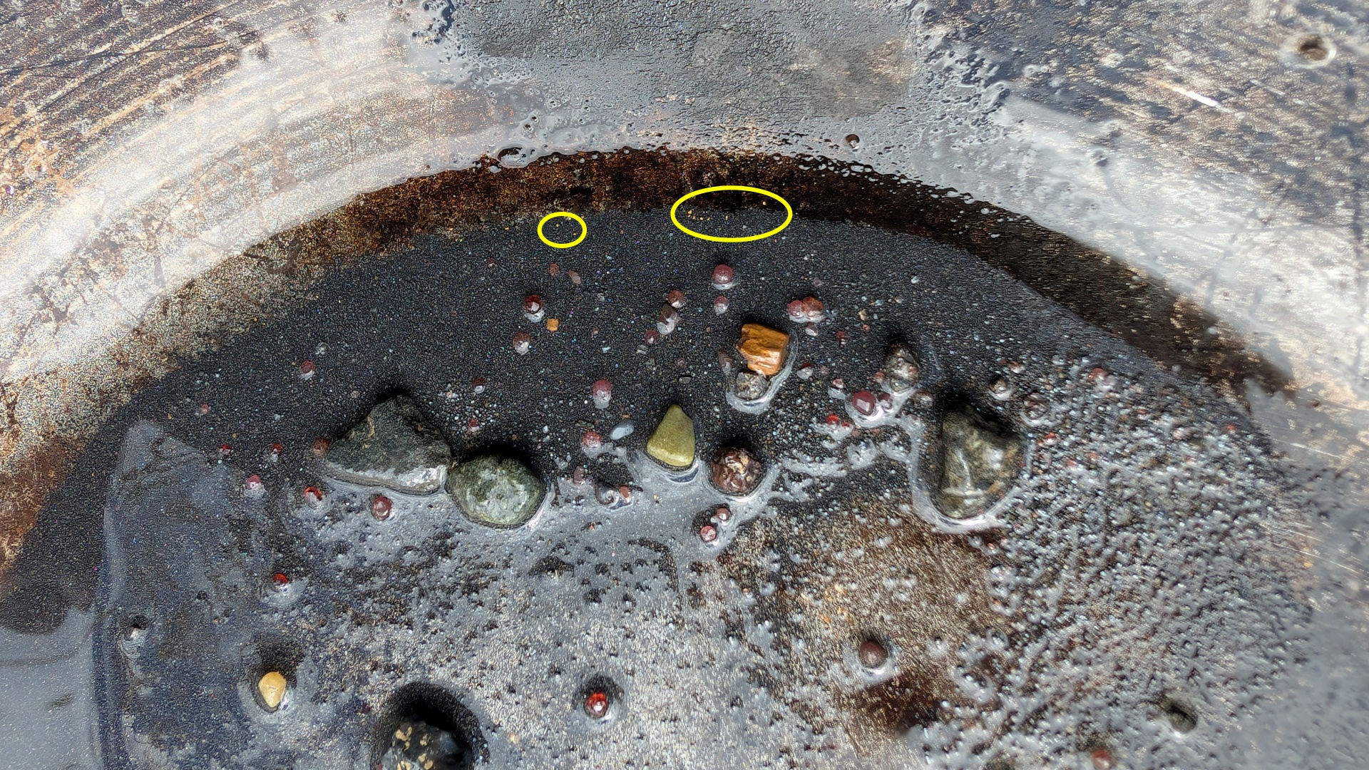 Mit gelben Kreis markierte Goldkrümel in schwarzem Sand