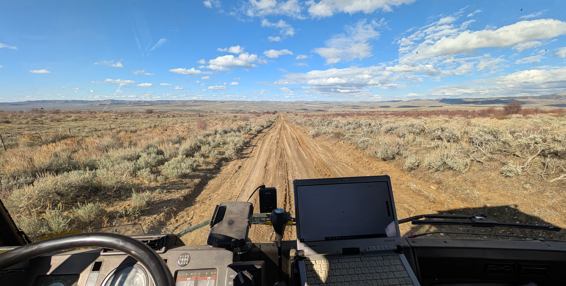Blick aus dem LKW auf eine lehmige Piste und blauem, wolkigen Himmel 
