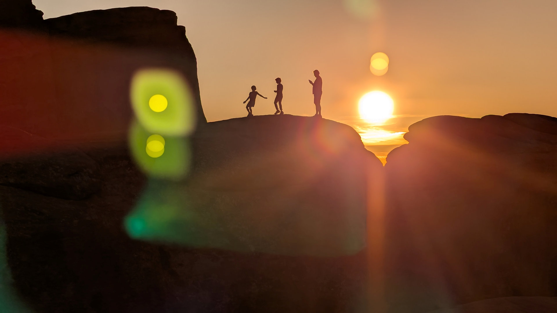 Drei Menschen klettern beim Sonnenuntergang auf einem Felsen herum 