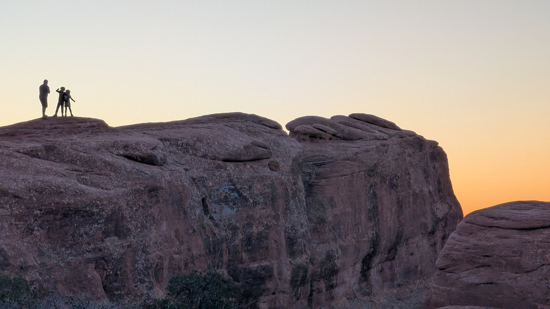 Vater fotografiert zwei Kinder bei Sonnenuntergang auf einem Felsen
