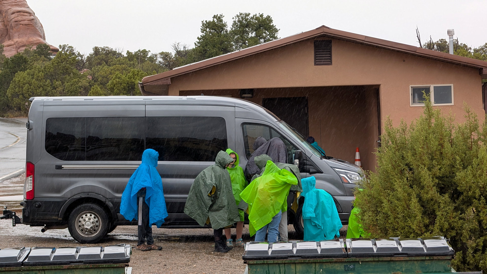 Eine Familie schützt sich mit bunten Regencapes vor einem Regenschauer