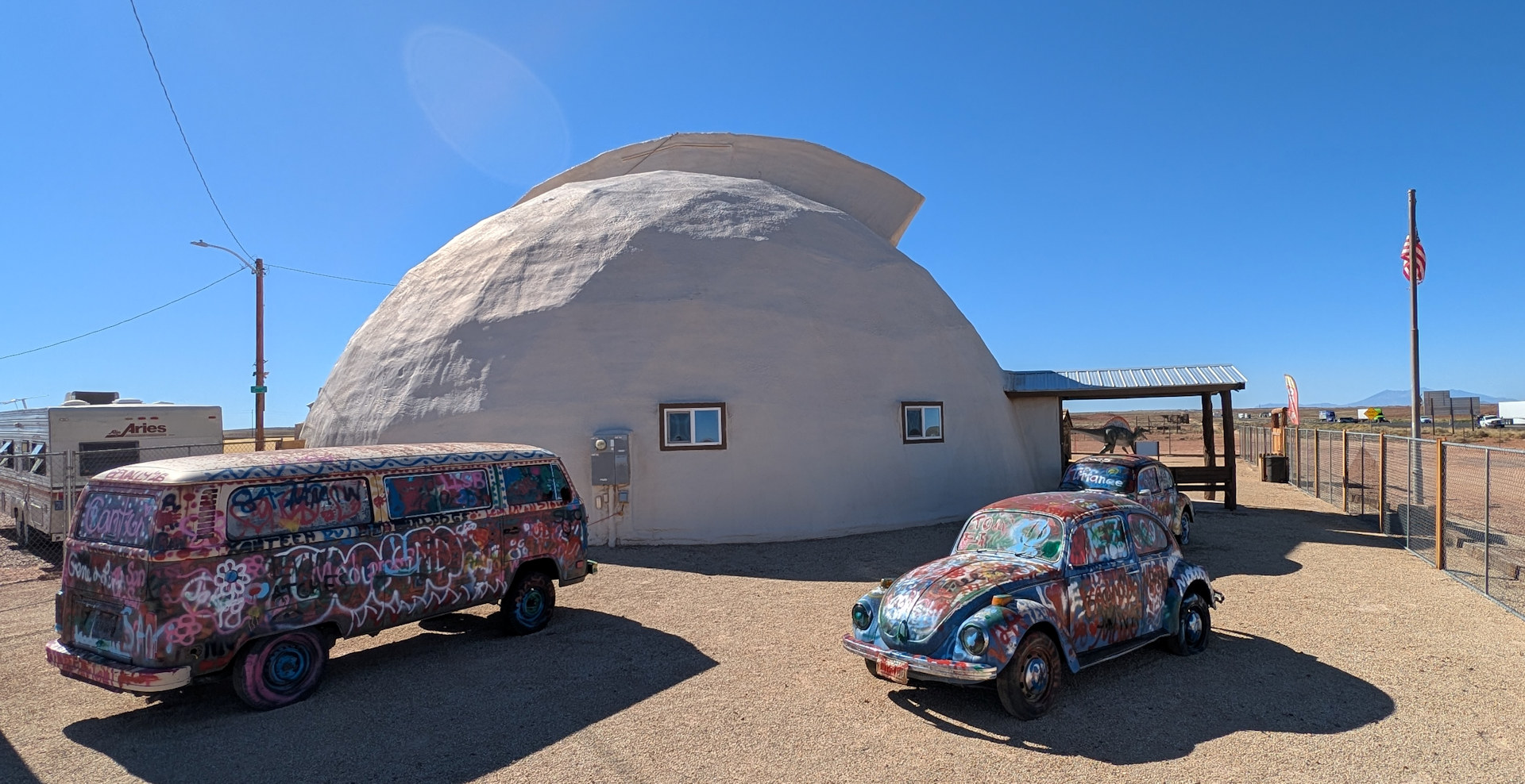 Bunt bemalter VW Bus und VW Käfer vor einem weissen halbkugelförmigen Gebäude mit zwei kleinen fenstern