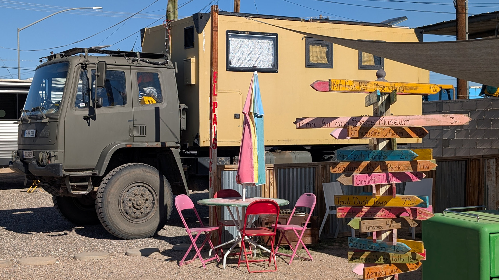 DAF T244 LKW, der hinter einem Campingtisch mit rosa Stühlen und einem Webweiser mit vielen Schildern parkt.