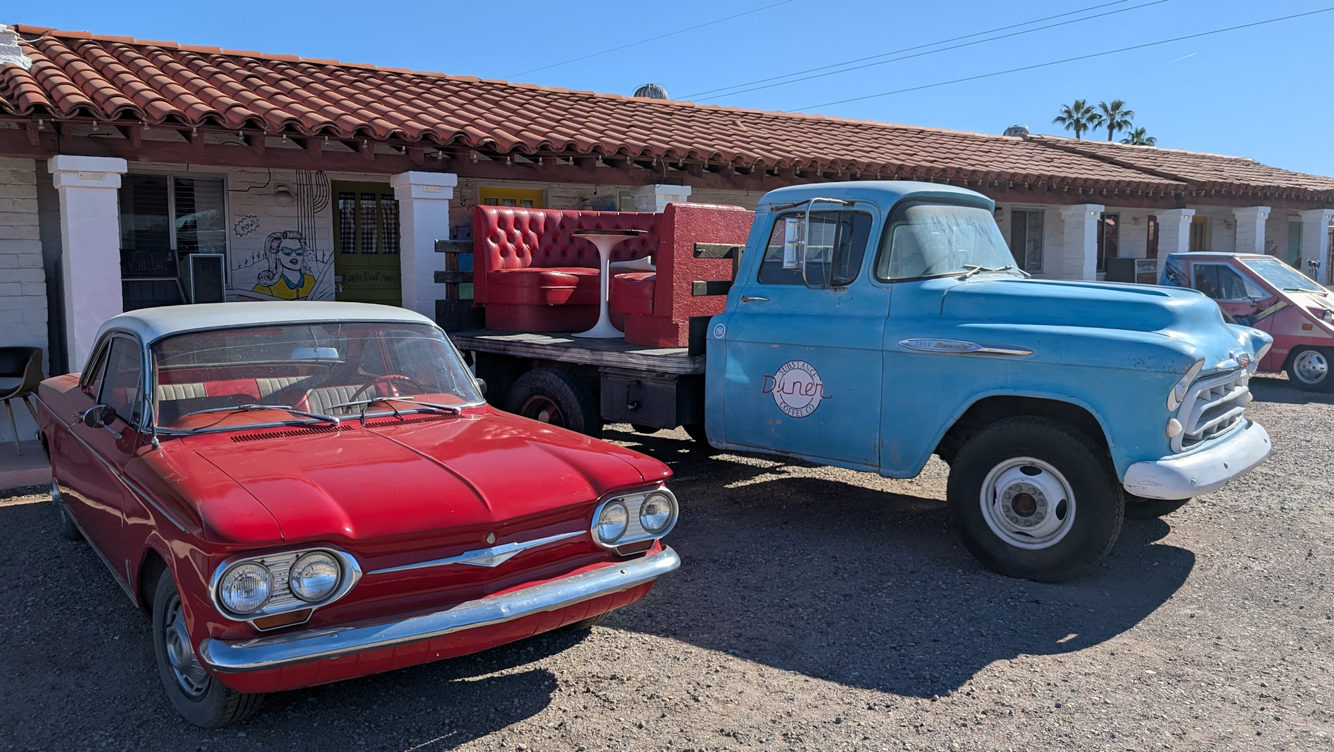 Ein roter Chevrolet Corvair und ein blauer Kleinlaster parken vor einem Motel