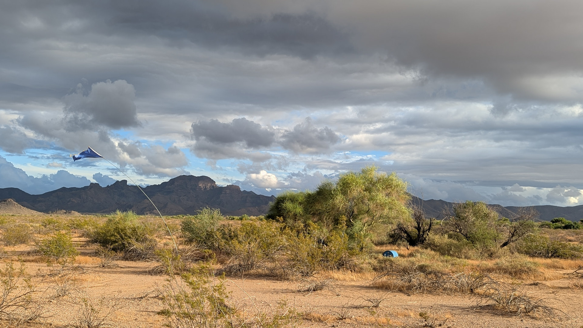Blaue Tonne mit blauer Fahne in einer dramatischen Wüstenlandschaft mit dunklen Wolken 