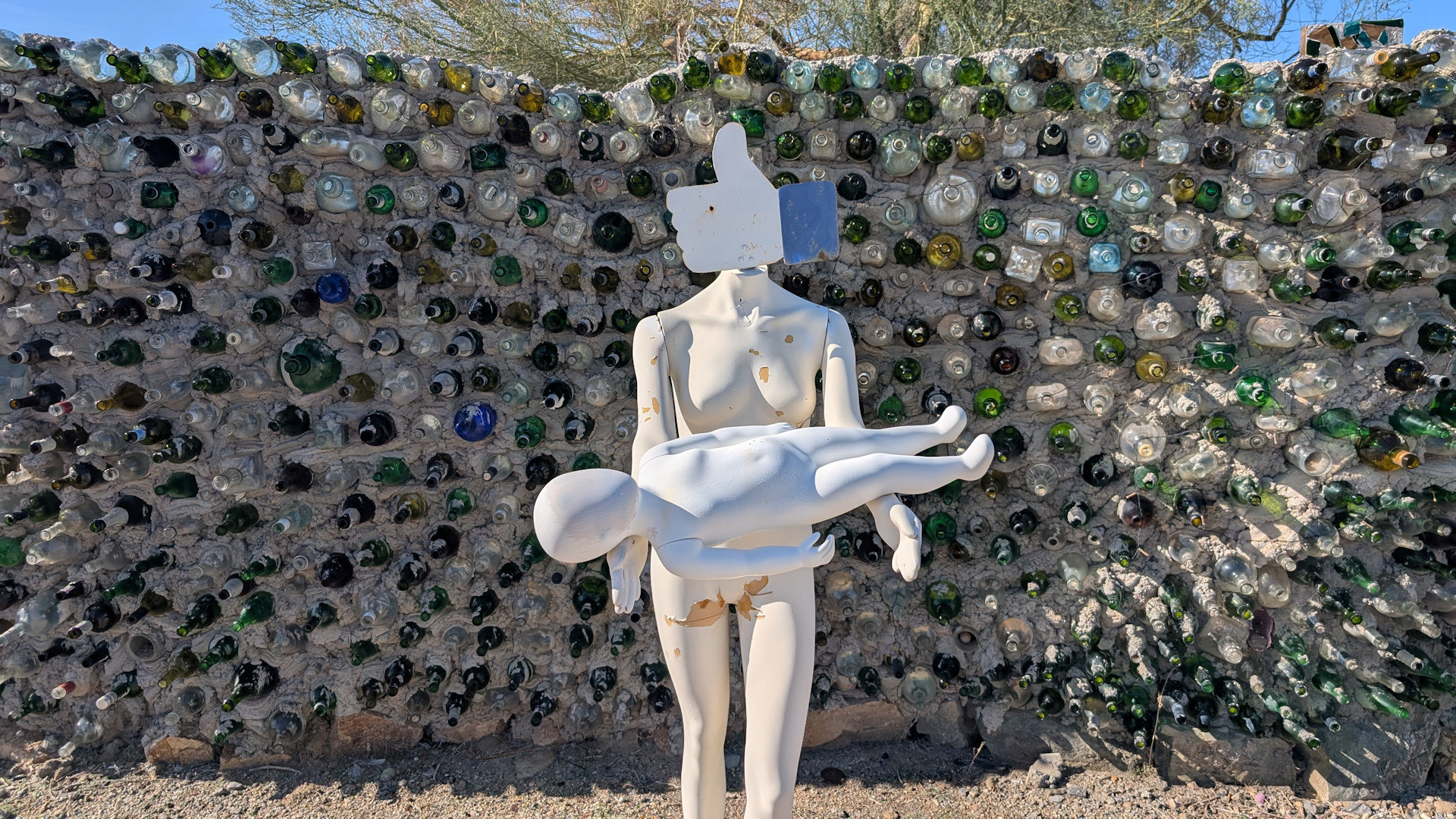 Eine weisse Schaufensterpuppe hält eine Plastikfugur in den Händen mit einem facebook like button als Kopf