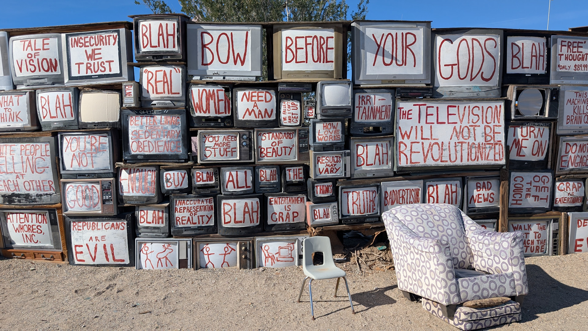 Wand ausgediente Fernseher mit weissen Tafeln und roten Botschaften darauf als mahnendes Kunstwerk in Slab City
