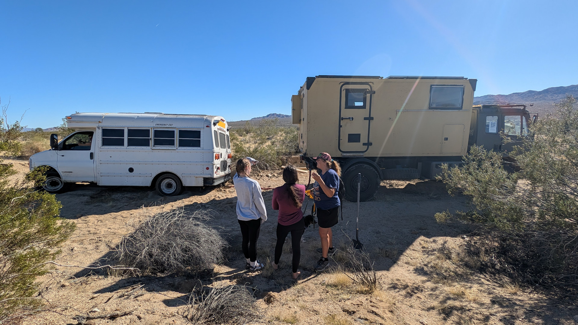 Drei Personen besprechen vor einem im Sand stecken gebliebenen Kleinbus und einem DAF T244 LKW die bevorstehende Bergung. 