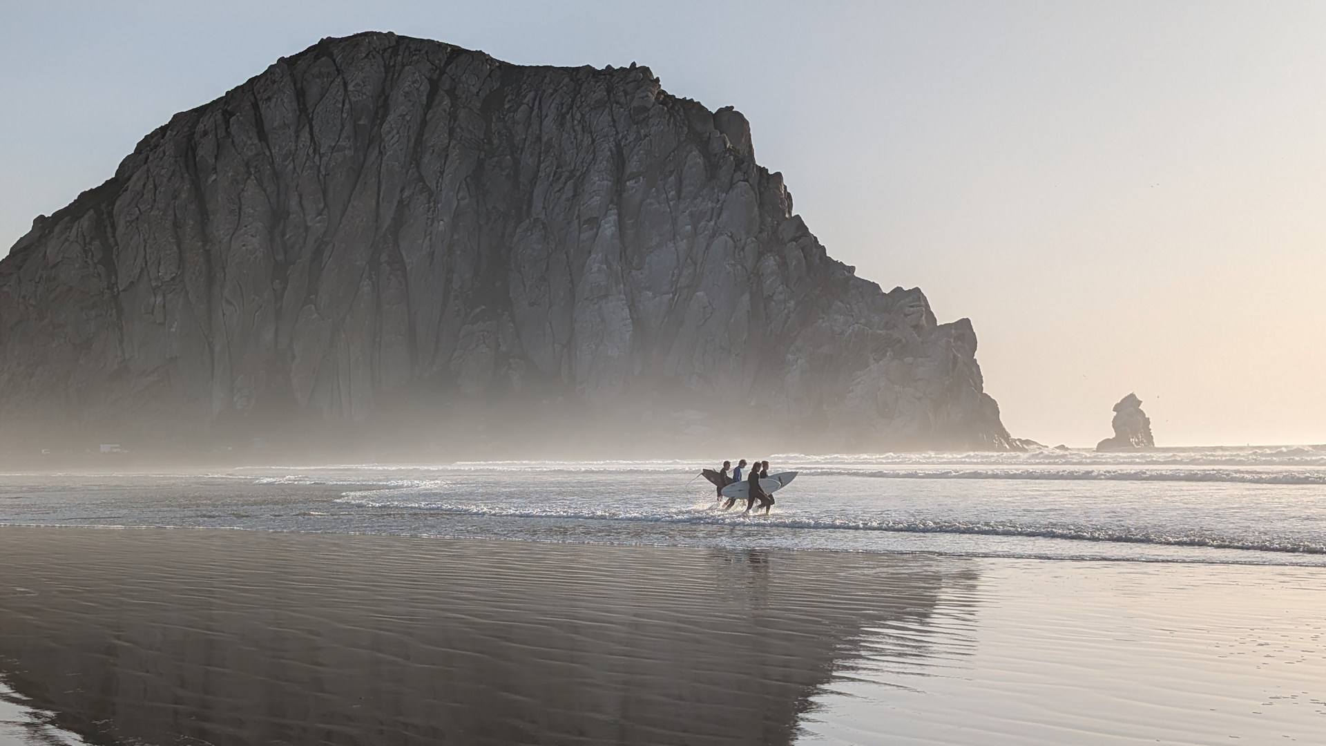 Vier Surfer laufen vor dem Morro Rock in Morrow Bay an der US 1 zum Meer