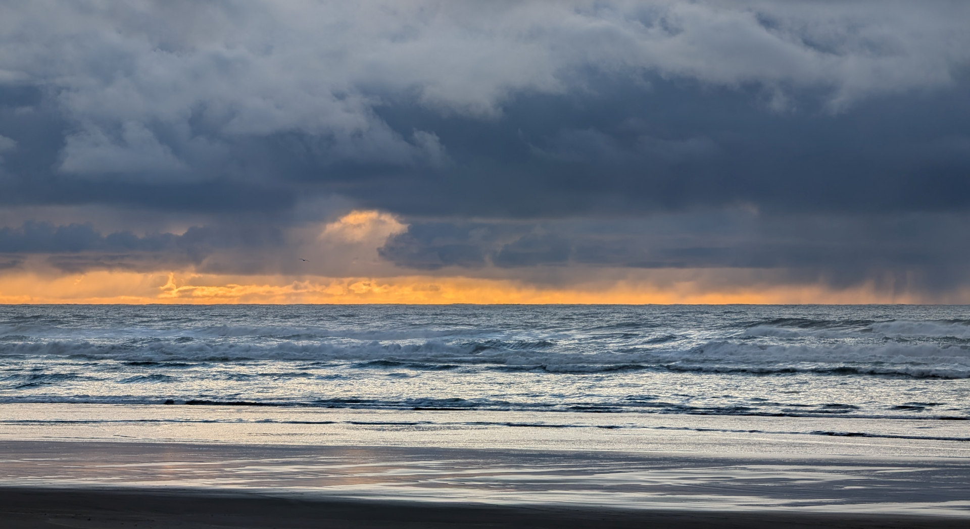 Küste mit gelben Wolkenstreifen und dunklen Wolken