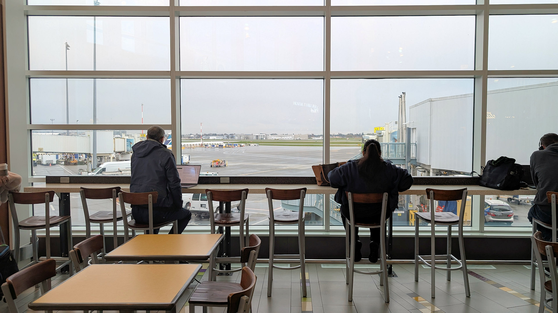 Öffentlicher Wartebereich für Gäste im Flughafen Vancouver mit Tischen Stühlen & Blick aufs Flugfeld