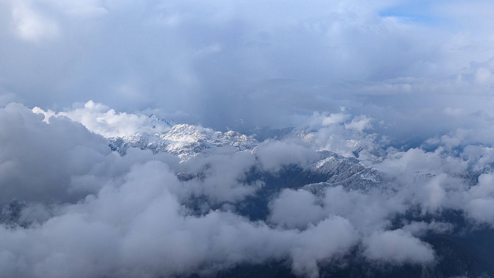 Schneebedeckte Berge Kanadas zwischen Wolken vom Flugzeug aus gesehen 