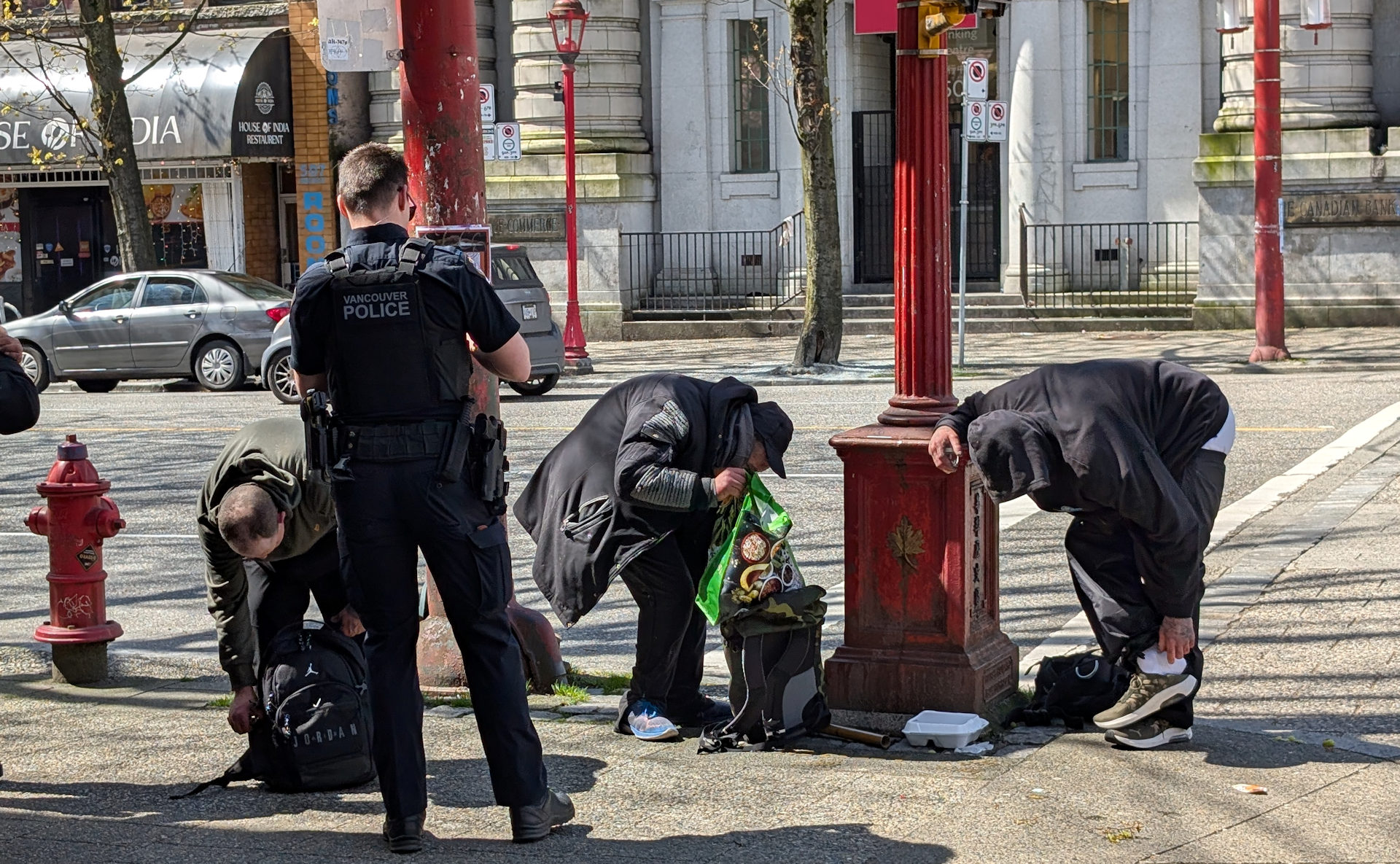 Ein Polizist kontrolliert in Vancouver drei Drogenabhängige die ihre Taschen ausleeren müssen