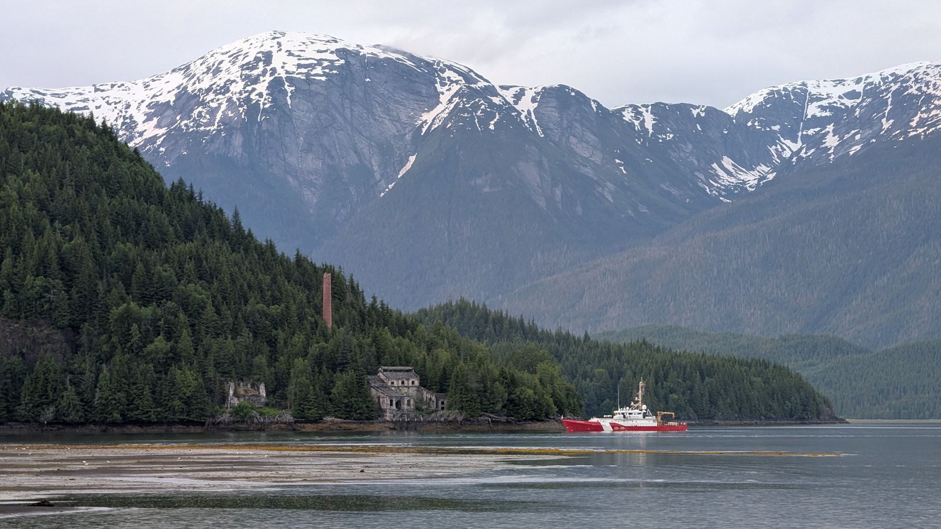 Rotes Schiff der Küstenwache ankert vor Ruinen in Anyox, mit schneebedeckten Bergen im Hintergrund