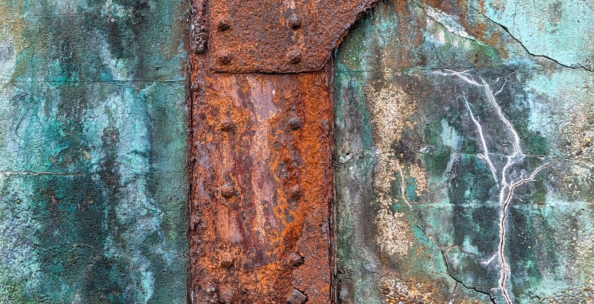 Rostige Metallstrebe vor einer Wand die türkis verfärbt ist