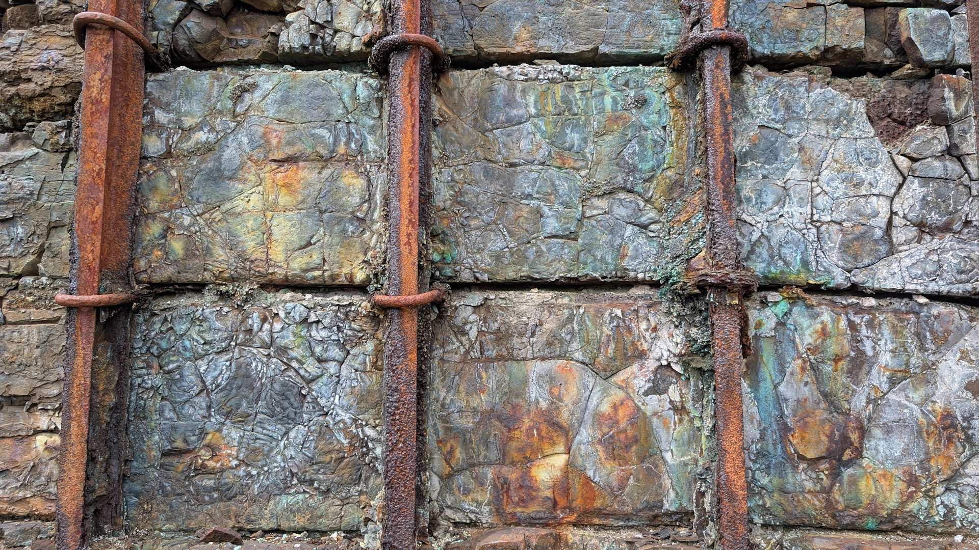 Rostige Metallstangen die an einer rostig bunt verfärbten Wand befestigt sind