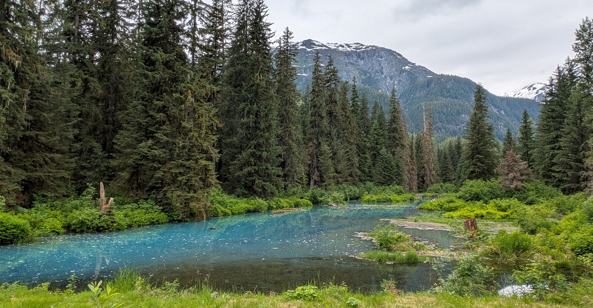 Blaue Lagune in Hyder. Kleiner blauer See mit schneebedeckten bergen und grünem Nadelwald