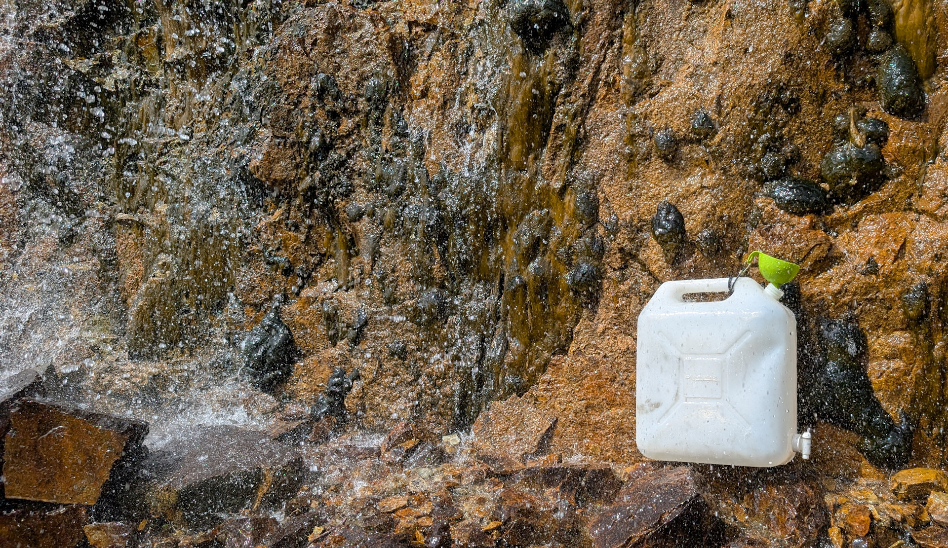 Wasserkanister der mit Hilfe von einem grünen Trichter an einem Wasserfall gefüllt wird