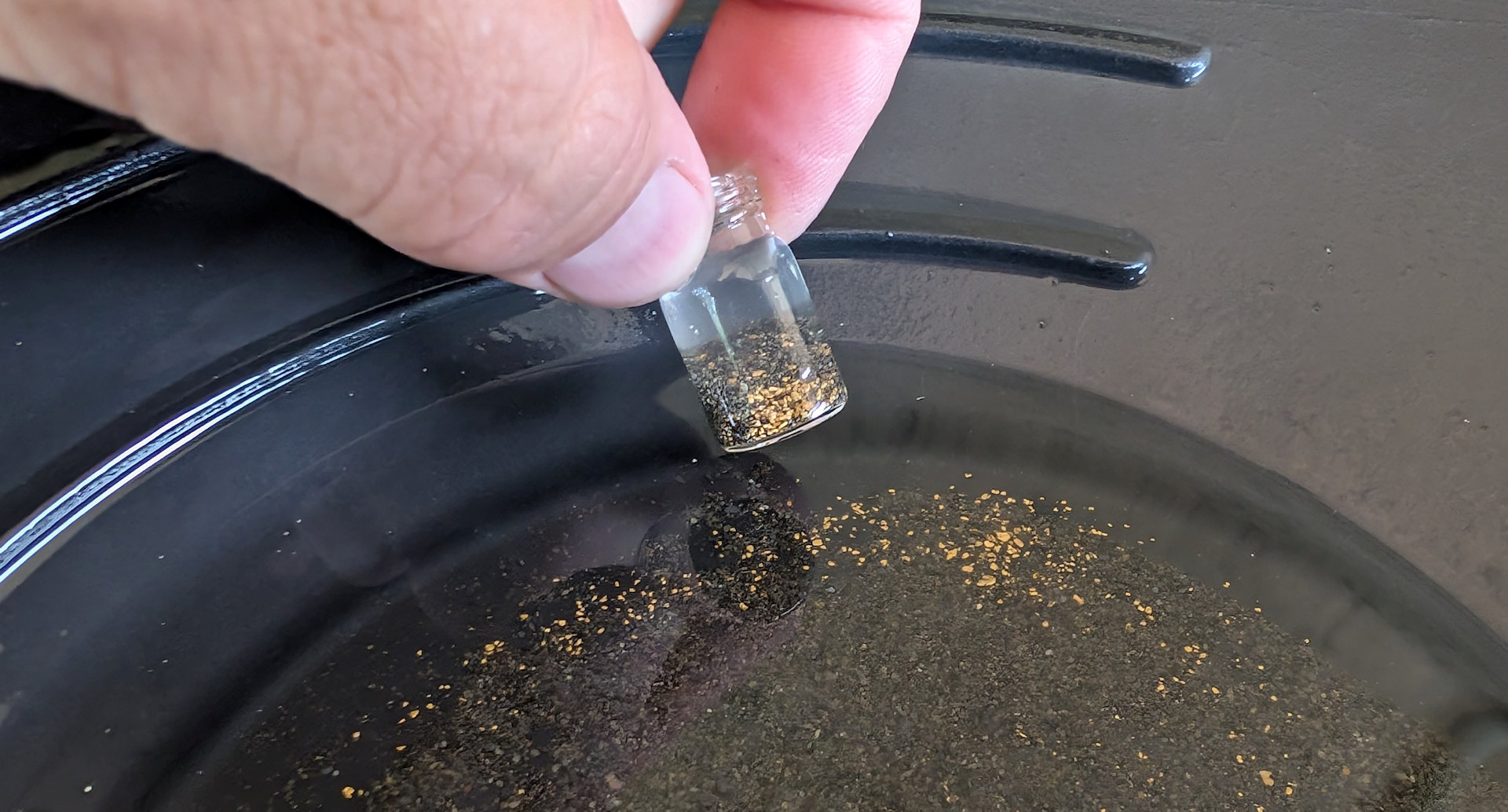 Kleines Glas mit Goldsand in einer Goldwaschpfanne mit viel Goldstaub darin 