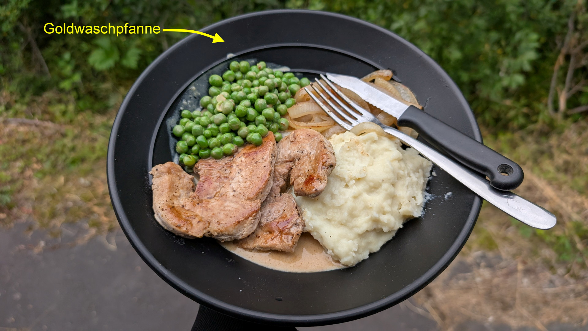 Menü aus Schweinefleischbraten, Kartoffel Püree und Erbsen serviert in einer schwarzen Goldwaschpfanne