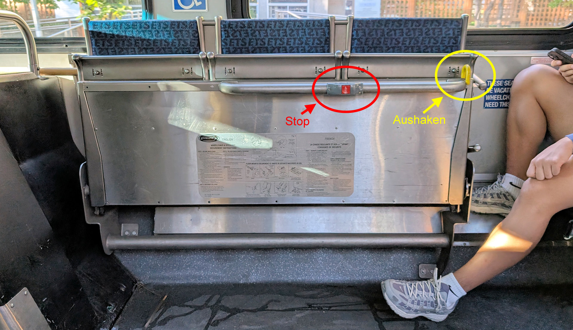 Hochgeklappte Bank in einem Bus mit Platz für Menschen im Rollstuhl. Der STOP Button und der helbe Haken zum auskaken der Bank wurde mit farbig markiert