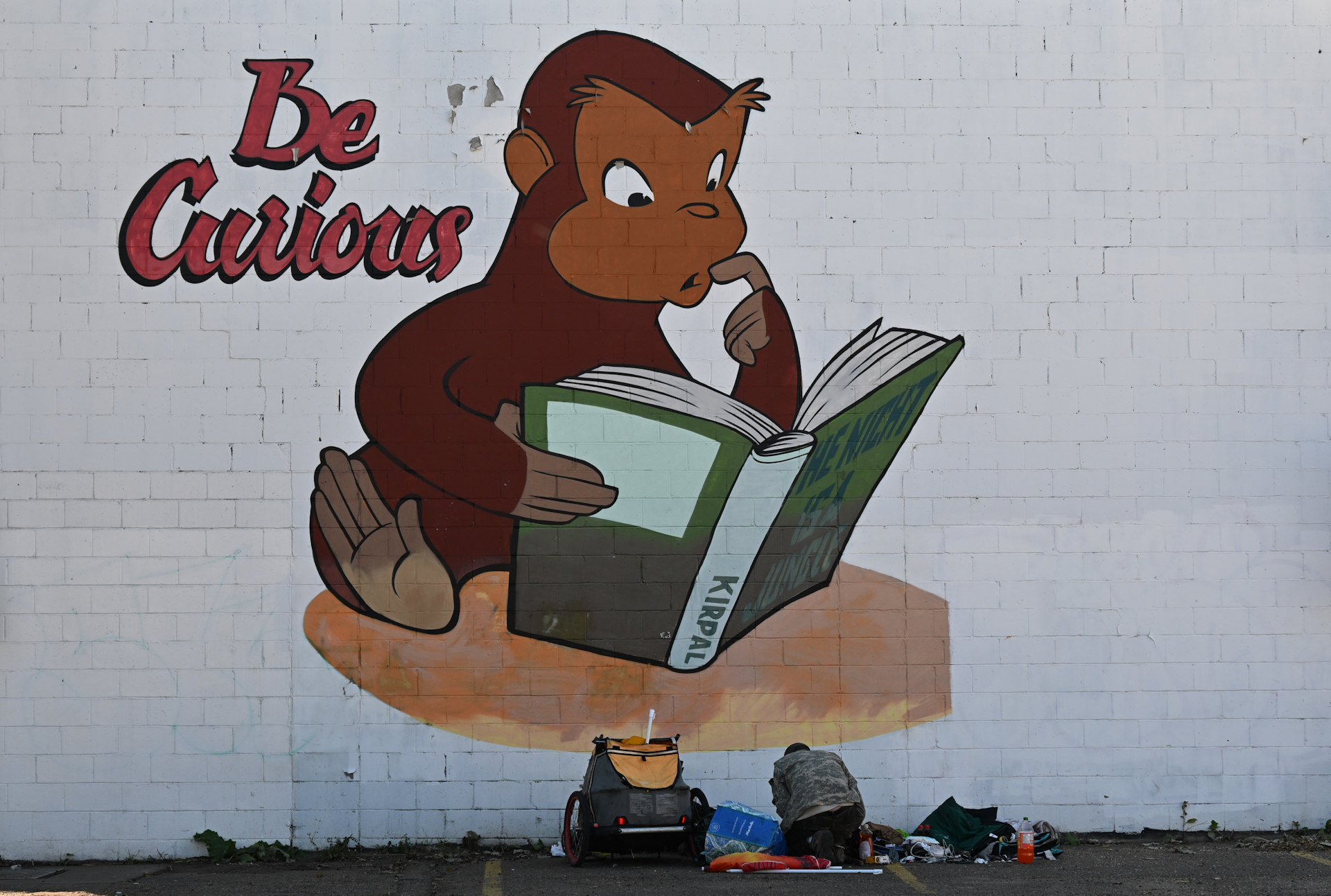 Graffiti mit einem neugierigen Affen, der ein Buch liest. Am Boden sitzt ein obdachloser Mann.  